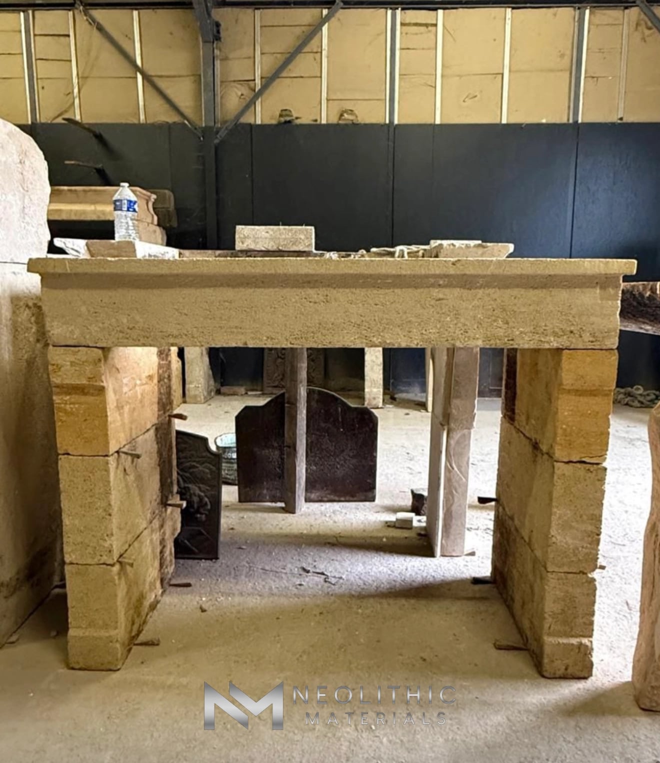 Reclaimed Fireplace Mantel FG105-19.ON slightly elevated eye-level interior photograph displaying an antique carved stone fireplace mantel assembly under warm indoor lighting, highlighting the classic tiered crown molding across the lintel resting on stacked structural stone side posts.