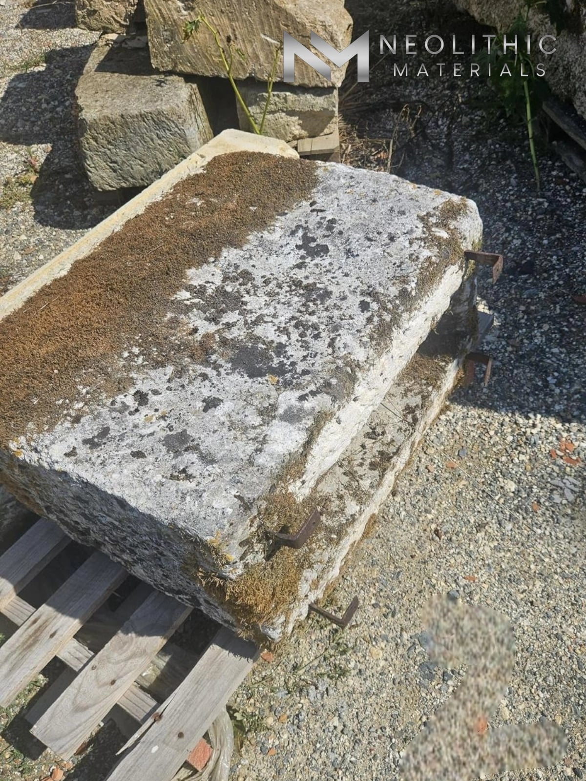 Trough FL101-02.MM side-angle outdoor perspective shot of a thick rectangular antique stone trough with a heavily distressed, lichen-encrusted grey-brown limestone surface resting on a wooden forklift pallet over a gravel lot under bright daylight.